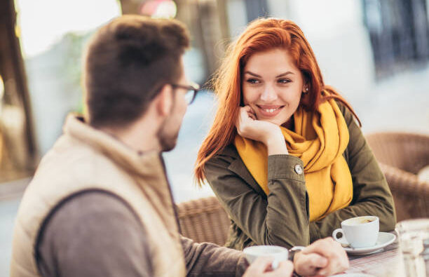 Attractive young couple in love sitting at the cafe table outdoors, drinking coffee