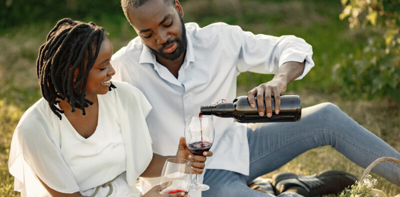 Carefree, relaxed couple enjoying the picnic together. Man poring wine into glass.