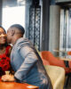 Couple enjoying day out at restaurant. Black man gifted a bouquet of red roses for a woman. Woman wearing red elegant dress and man blue costume.